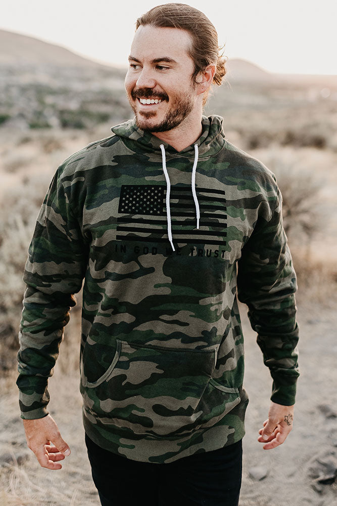 Man wearing the camo In God We Trust hoodie outdoors