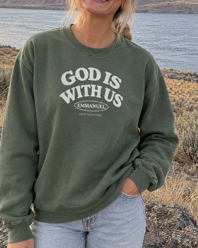 Emmanuel God With Us Crewneck Sweatshirt - close-up of the Military Green crewneck's white God Is With Us print worn by a blonde woman by the Columbia River