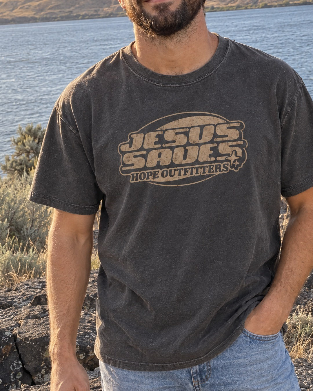 Jesus Saves Retro Tee - close-up of the graphite tee's tan Jesus Saves print, worn by a bearded man by the Columbia River