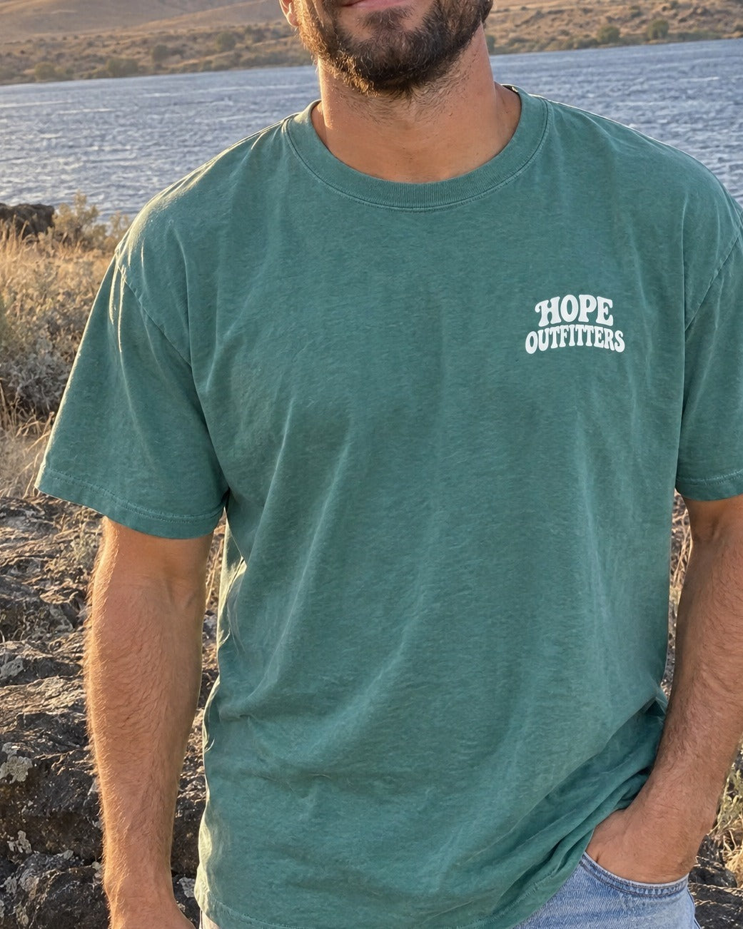 No Other Name But Jesus Tee - close-up of the small Hope Outfitters chest logo on the emerald tee worn by a bearded man