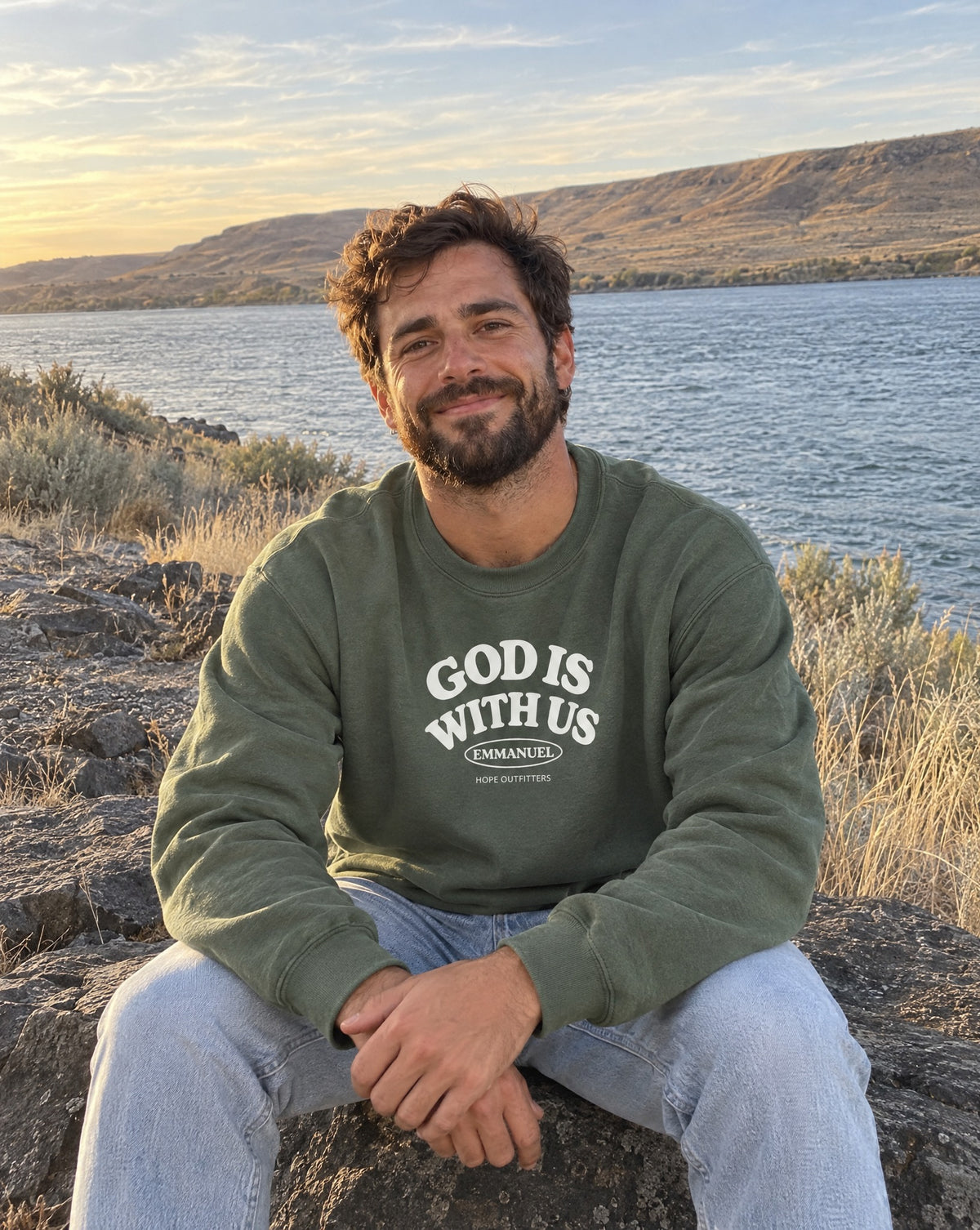 Emmanuel God With Us Crewneck Sweatshirt - bearded man sitting on basalt by the river in the Military Green crewneck