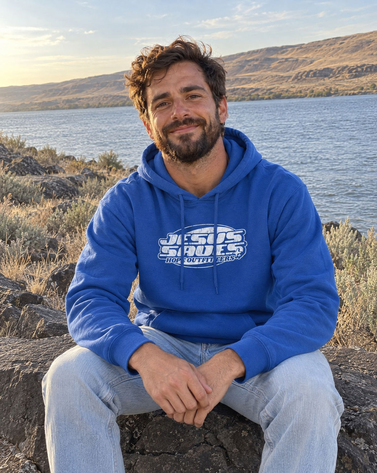 Jesus Saves Retro Hoodie - bearded man sitting on basalt by the river in the Royal blue hoodie