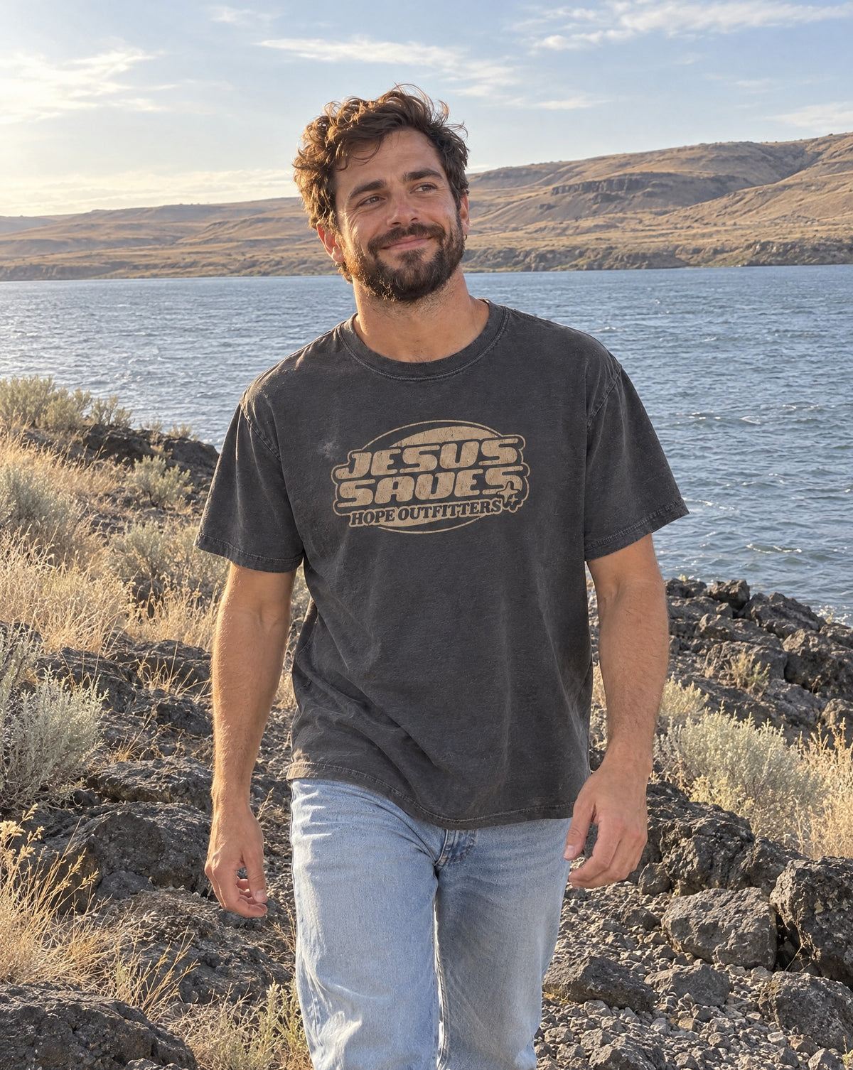 Jesus Saves Retro Tee - bearded man walking along basalt rocks at the Columbia River's edge in the graphite tee