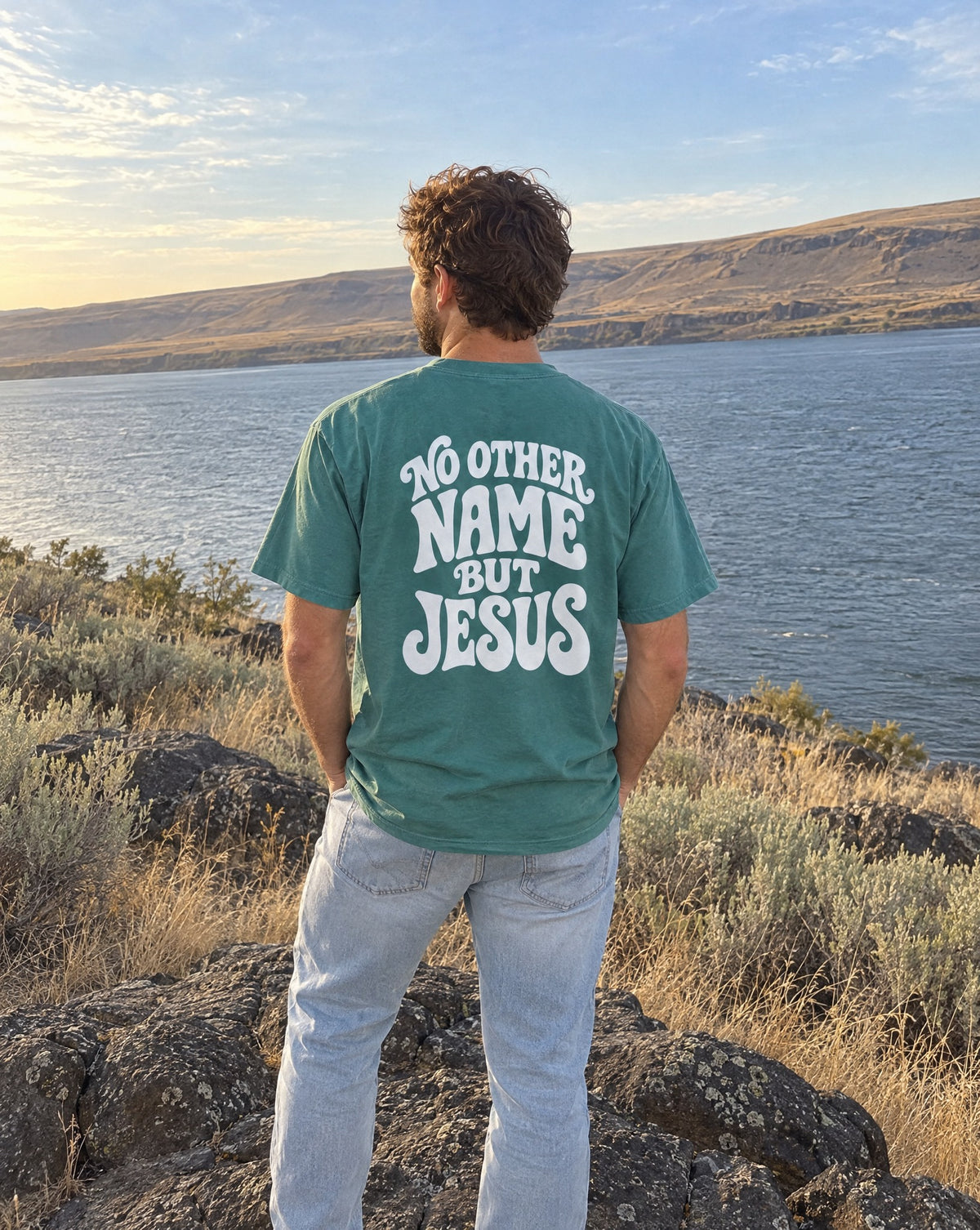 No Other Name But Jesus Tee - man seen from behind on a basalt boulder looking at the Columbia River, back print visible
